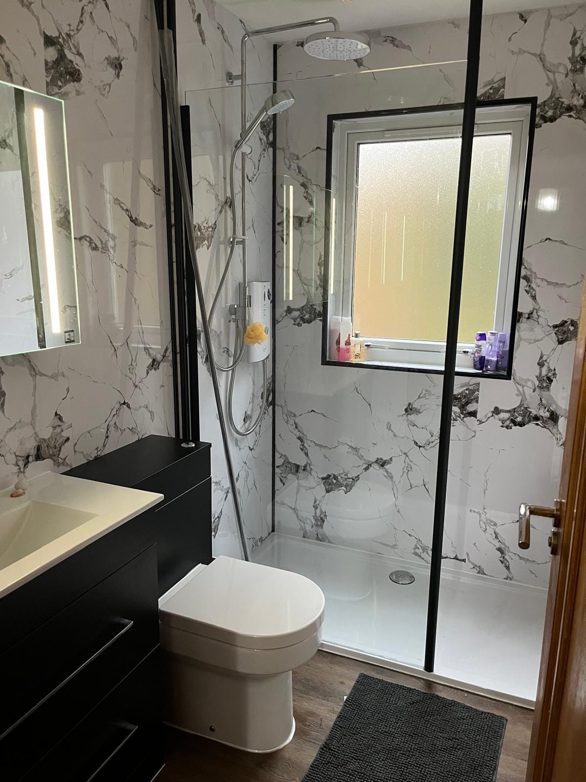 The walk-in shower at Barra Woodview — black-framed glass screen with rainfall and handheld heads