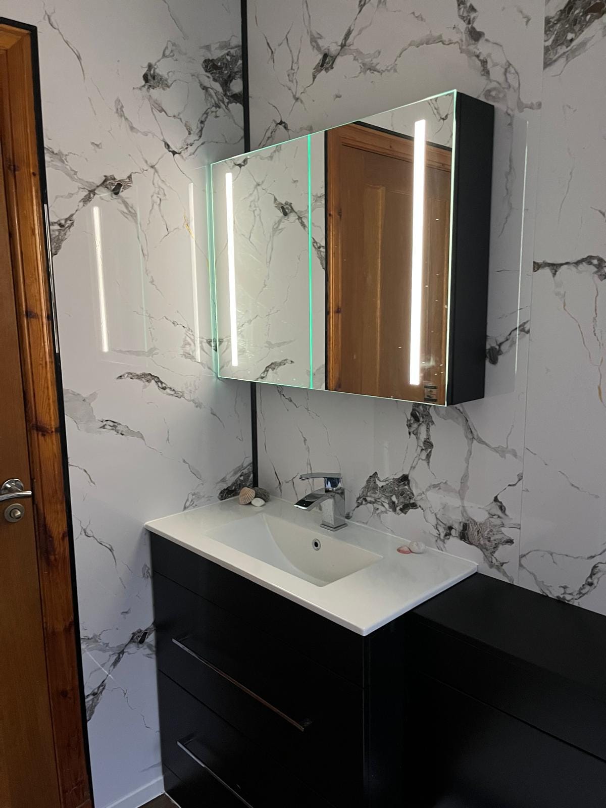 White basin on a black vanity unit with an LED-lit mirror cabinet above